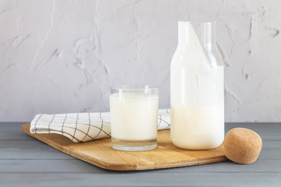 Vintage jar with cork of homemade yogurt, kefir, fermented milk or sour cream next to drinking glass and wooden spoon on kitchen table