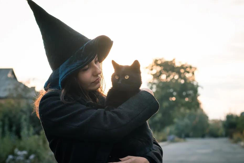 woman in a witch costume holding a black cat