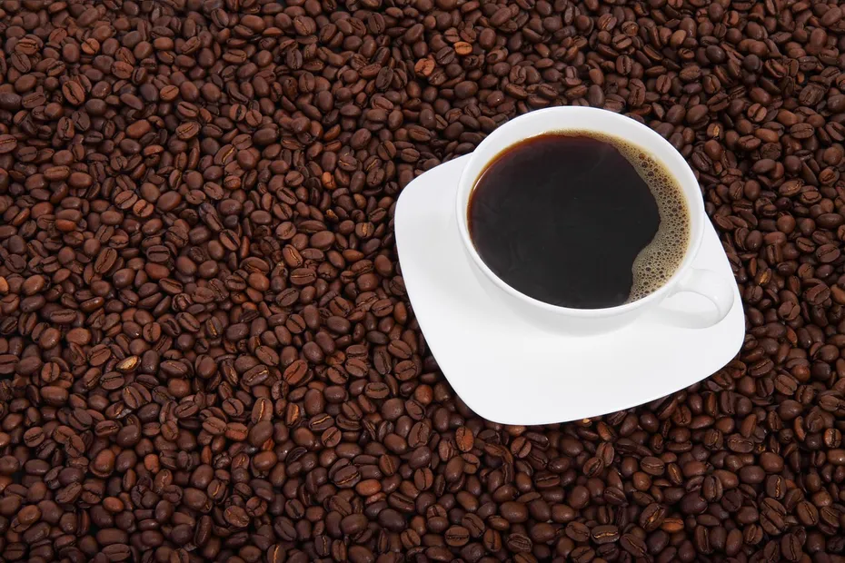 cuo of black coffee placed under a bed of coffee beans