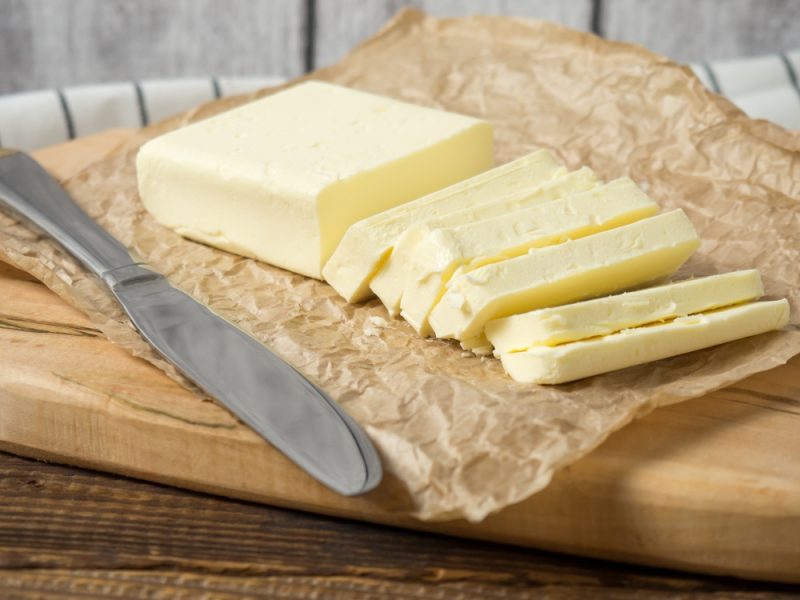 Fresh butter block sliced on wooden cutting board