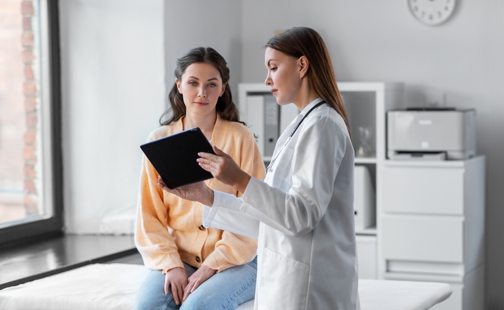 female doctor with tablet pc computer talking to woman patient at hospital
