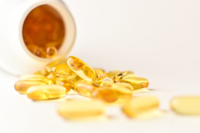Omega 3 fish oil capsules spilling out of a bottle on a white background